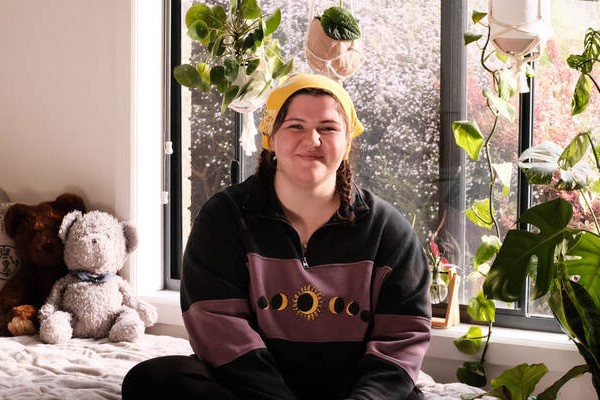 Tara, a young person who has benefited from Canteen's free cancer support services for young Australians, smiling into the camera in front of a window