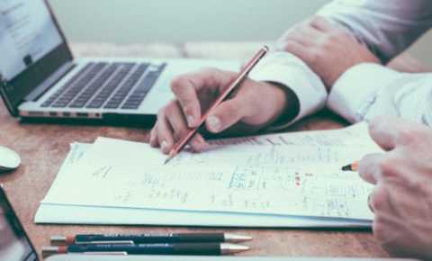 Image of hands writing on a paper next to a laptop 
