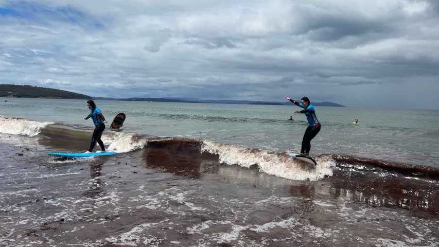 two young people trying surfing at dodges ferry in tasmania with canteen